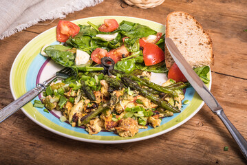 Fried scrambled eggs with asparagus, spinach and tomatoes in a large plate on a rustic wooden table - a simple rustic breakfast