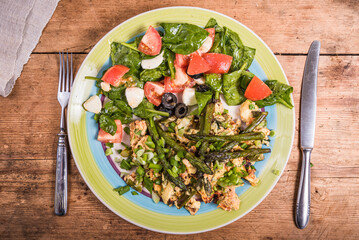 Fried scrambled eggs with asparagus, spinach and tomatoes in a large plate on a rustic wooden table, top view, close-up - simple rustic breakfast