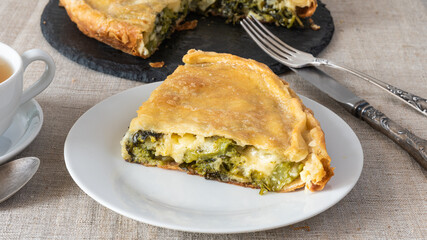Piece of pie and pie itself with cheese and broccoli with fork and knife, close up