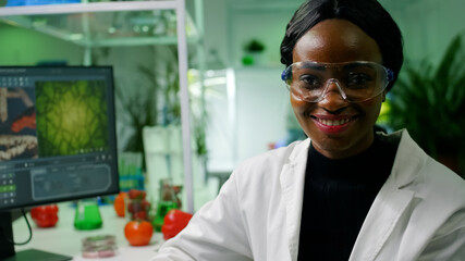 Close up of african biologist doctor wearing medical equipment smiling at camera while sitting in...