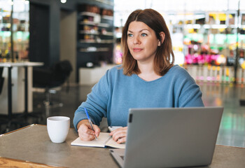 Beautiful stylish young woman plus size body positive using laptop at beauty salon office, small business owner