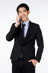 Portrait shot of Asian young happy handsome smart office worker leader in black formal suit with necktie standing smiling talking with client on mobile smartphone in hand in front of white background