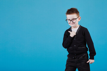 Like. Portrait of happy little schoolboy with glasses smiling at camera and doing thumbs up gesture, showing agree cool approval sign. indoor studio shot isolated on blue background