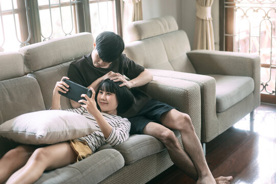 Young adult asian lover couple sitting on sofa and play game cozy style indoor on day.