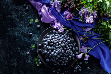 Summer still life with blueberries, colored sweet peas and meadow grasses on a dark blue table.