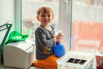 Little Caucasian boy 2 years old watering seedlings from a spray