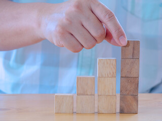 Hand arranging wood cube stacking as stair step shape on wooden table .Business concept create symbol or logo, development, growth and management concept.