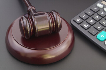 Wooden judge gavel and calculator on black table close up