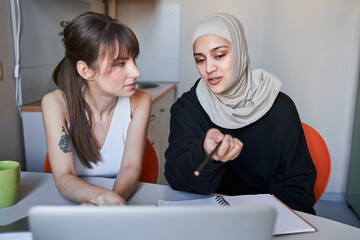 Woman wearing hijab pointing with her finger to the laptop screen while explaining something