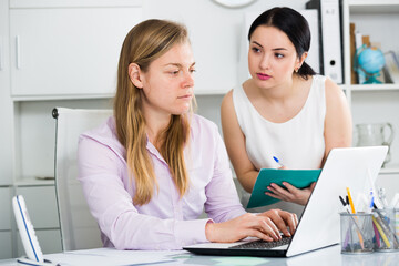 Female senior manager examining work of woman newcomer in office