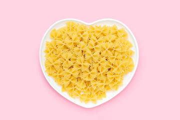 Raw farfalle in a heart shape plate on a pink background, uncooked pasta butterfly or bow tie, Italian and Mediterranean cuisine an ingredient made from whole grain durum flour, healthy diet food