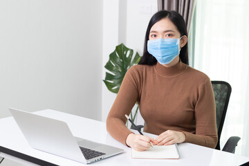 Young business asian woman working from home with laptop, wearing protective mask during self-isolation and quarantine. Coronavirus outbreak and flu covid epidemic.