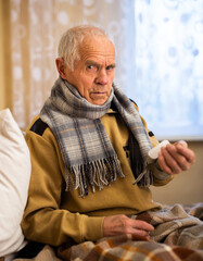 old man wrapped in blanket measuring pressure with tonometer