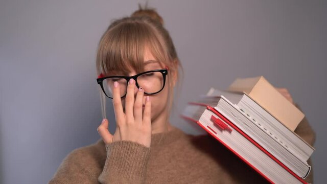 Nerd girl correcting eyeglasses. Attractive university or college blonde caucasian student girl in beige sweater holding stack of books in hands. Education or knowledge concept. 4k footage