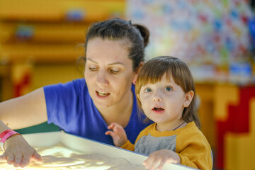 Creative early baby development. A mother teaches her child to draw with her fingers in the sand. Center for the Development of Children with Autism.