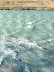 Turquoise waters with white foam and bank with grass of Sochi river.. Mountain river with clear water flows from Caucasus mountains. Sochi, Russia.