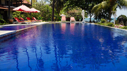 luxury hotel with swimming pool, sun beds, palm trees by sea. tropical resort with pool. Travel concept.