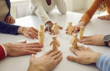 Team of multiracial business people and workmates sitting around white office table put little wooden human figures in circle as symbol of group, community, help, collaboration and teamwork - obrazy, fototapety, plakaty