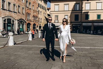 A romantic walk of the bride and groom through the streets of a European city. Bride with a bouquet of roses. Newlyweds travel to Italy.