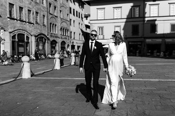 A romantic walk of the bride and groom through the streets of a European city. Bride with a bouquet of roses. Newlyweds travel to Italy. Black and white photo.