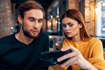 a woman in a sweater with a mobile phone and a guy with a beard are sitting in a restaurant