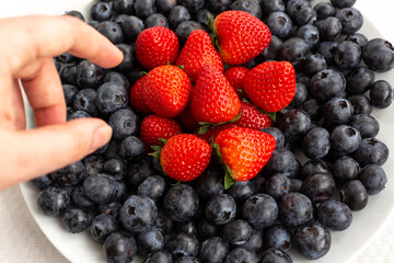 hand reaches for a plate of blueberries and strawberries