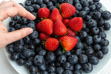 hand reaches for a plate of blueberries and strawberries