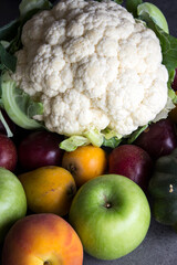 Colorful vegetables and fruits on gray textured background. Top view photo of cauliflower, apples, peach, avocado, plums. Eating fresh concept. 