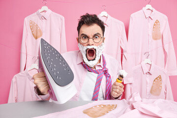Stressed European man yells loudly holds electric steam iron and shaving brush poses near ironing...