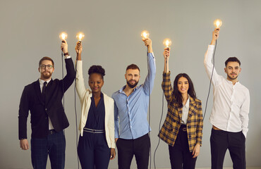 Group of happy creative young multiethnic business professionals holding up glowing light bulbs...
