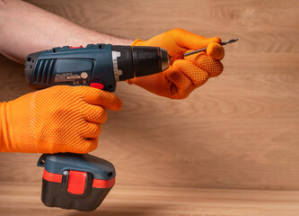 Male hand in building gloves holding professional cordless drill tool or machine for using in...