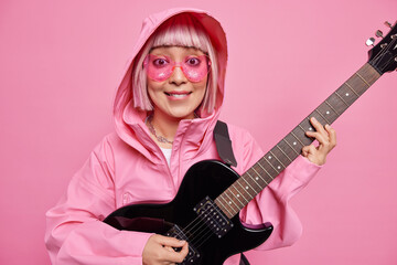 Fashionable woman with pink hair pretends performing on stage plays rock and roll music wears heart...
