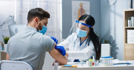 Close up portrait of pretty Asian female doctor in medical mask and face shield working in clinic...