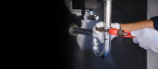 Plumber fixing white sink pipe with adjustable wrench.