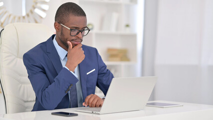 Fototapeta na wymiar Pensive African Businessman Thinking and Working on Laptop 