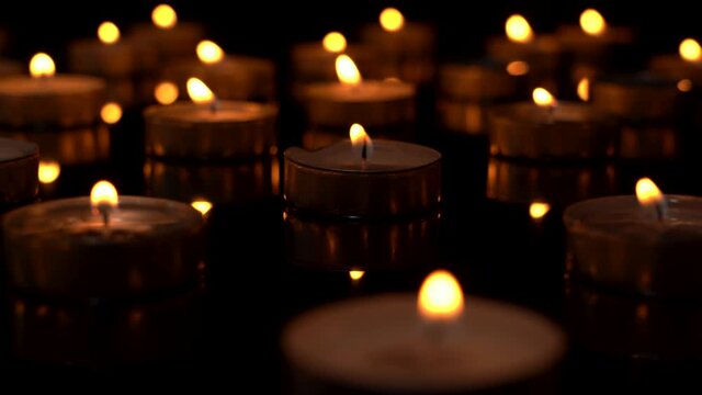 Many small candles burn on a black background