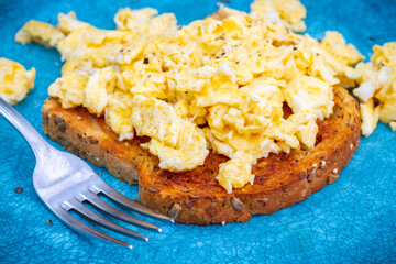 Srambled eggs on toast with pepper on top on a turquoise plate with a fork