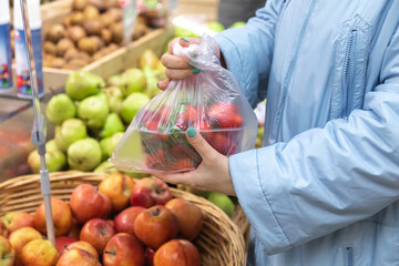 A woman packs strawberries in her bag. Shopping at the grocery store. Healthy eating.
