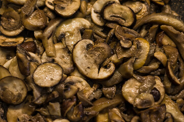 Plano cerrado de un conjunto de hogos laminados que son salteados con aceite de oliva en una sartén. 