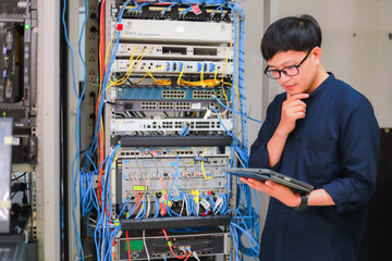 A young man using a tablet stood in the network server room while examining the server.