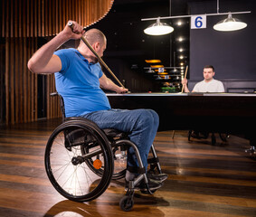 Adult men with disabilities in a wheelchair play billiards in the club