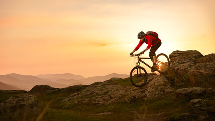 Naklejka na ściany i meble Cyclist in Red Riding Bike on the Summer Rocky Trail at Sunset. Extreme Sport and Enduro Biking Concept.