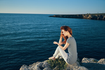 Naklejka premium woman in a t-shirt and trousers sits on a rock on the beach near the sea top view