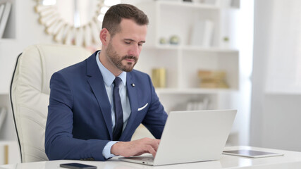 Serious Businessman using Laptop in Office 