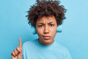 Serious dissatisfied mixed race young woman with Afro hair points index finger above uses...