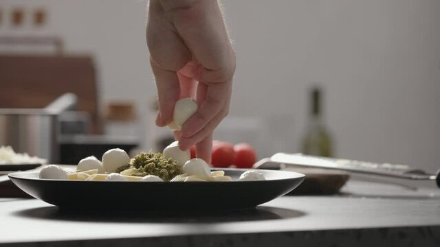 Slow motion orbit shot of man add mozzarella balls to pesto penne on black plate
