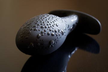 A black silicone butt plug with drops of moisture lies on a dark reflective surface. The concept of...