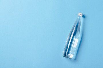 Glass bottle with clear water on a blue background. Concept of health and beauty, water balance, thirst, heat, summer. Flat lay, top view