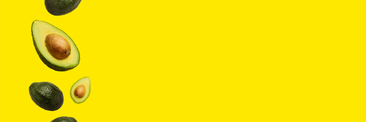 pitted avocado and whole avocado fly in the air on a yellow background. Top view, flat lay. Banner