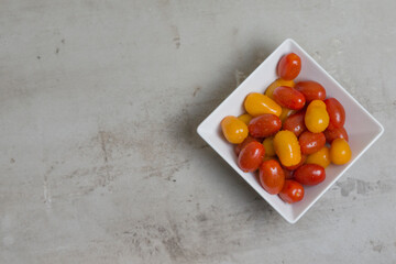 red and yellow small tomatoes in white square bowl. Flatly 